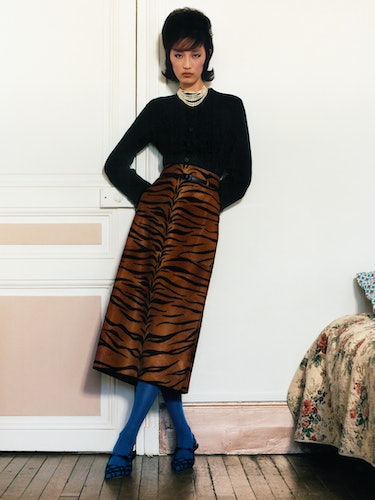 Xiru Yang wears a black jacket, tiger striped skirt, necklace; blue tights and black shoes.