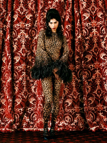 Cosma wears a leopard print dress, tights, earrings; black shoes.