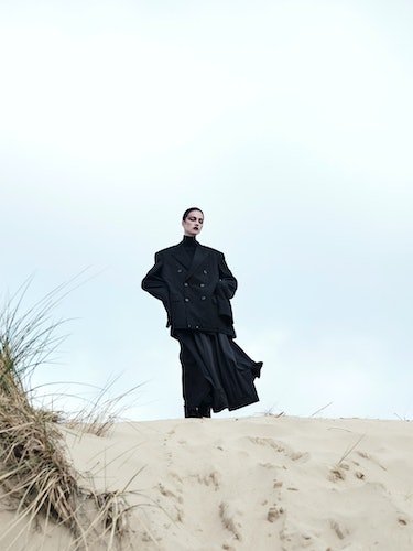 Model wears a black men's blazer, black turtleneck, black skirt.